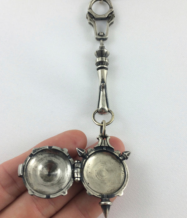 A silver-toned metal locket pendant with a lobster clasp, decorative stem, and round locket-style pendant shown open and held in a hand against a white background.