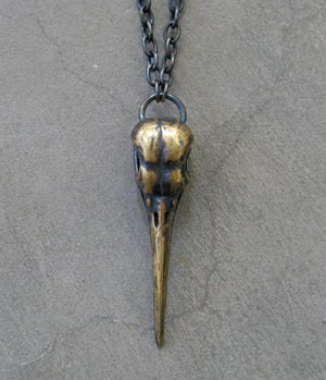 A solid brass pendant necklace featuring a bird skull design, with a gold-toned finish and a chain link.