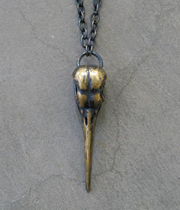 A solid brass pendant necklace featuring a bird skull design, with a gold-toned finish and a chain link.