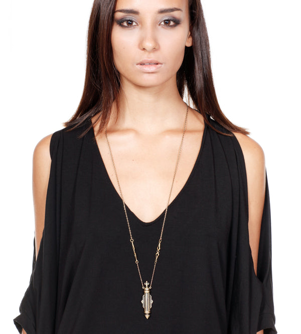 Woman wearing a black top and a long necklace with a pendant on a white background